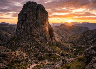 Hiker on a rocky trail near a large monolithic rock formation with a colorful sunset sky