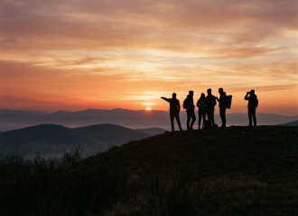 Silhouetted group of people standing on a hilltop watching sunset over distant hills