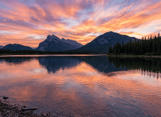 Sunset sky reflecting on calm lake with mountain silhouettes and pine forest